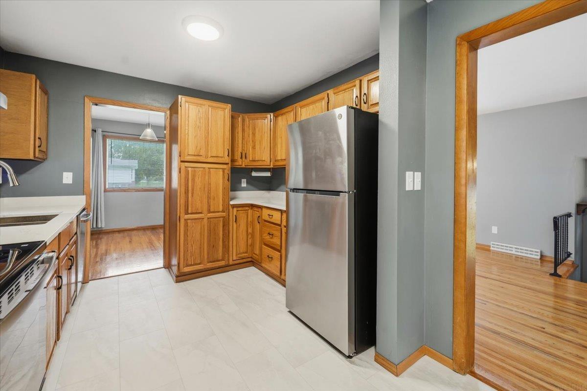 Kitchen with honey-toned cabinets, stainless steel refrigerator, and tile floor