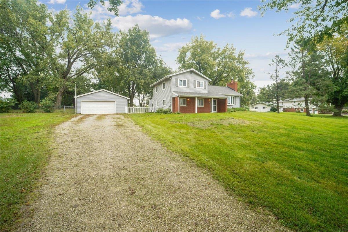 Two-story gray-and-brick home beside a detached garage, with a gravel driveway and broad lawn.