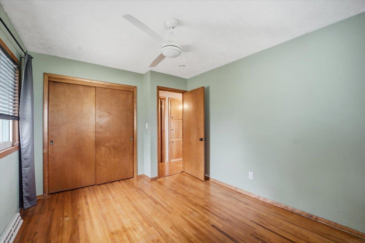Unfurnished bedroom with hardwood floors, a wooden sliding-door closet, and a ceiling fan.