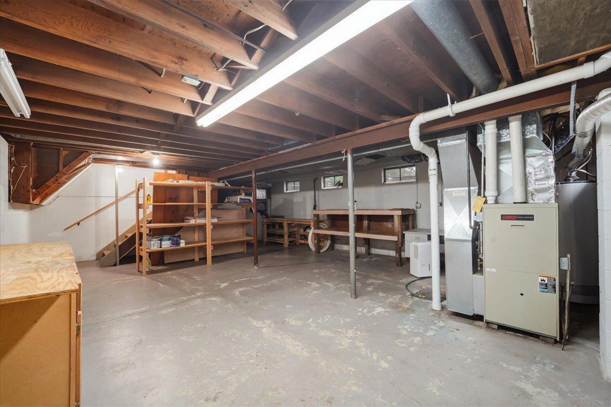 Unfinished basement with exposed ceiling joists, storage shelves, a workbench, and furnace.