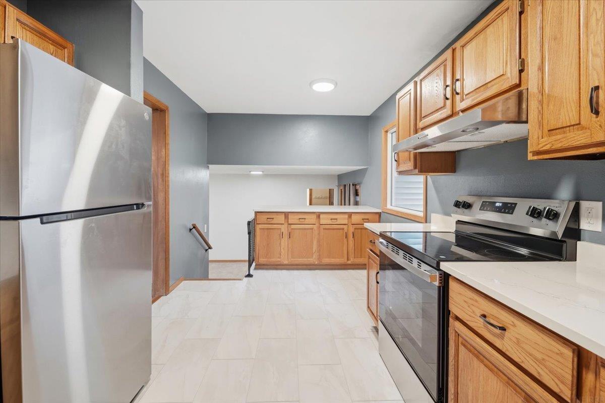 Kitchen with honey-colored wood cabinets, pale tile floors, and stainless steel appliances.