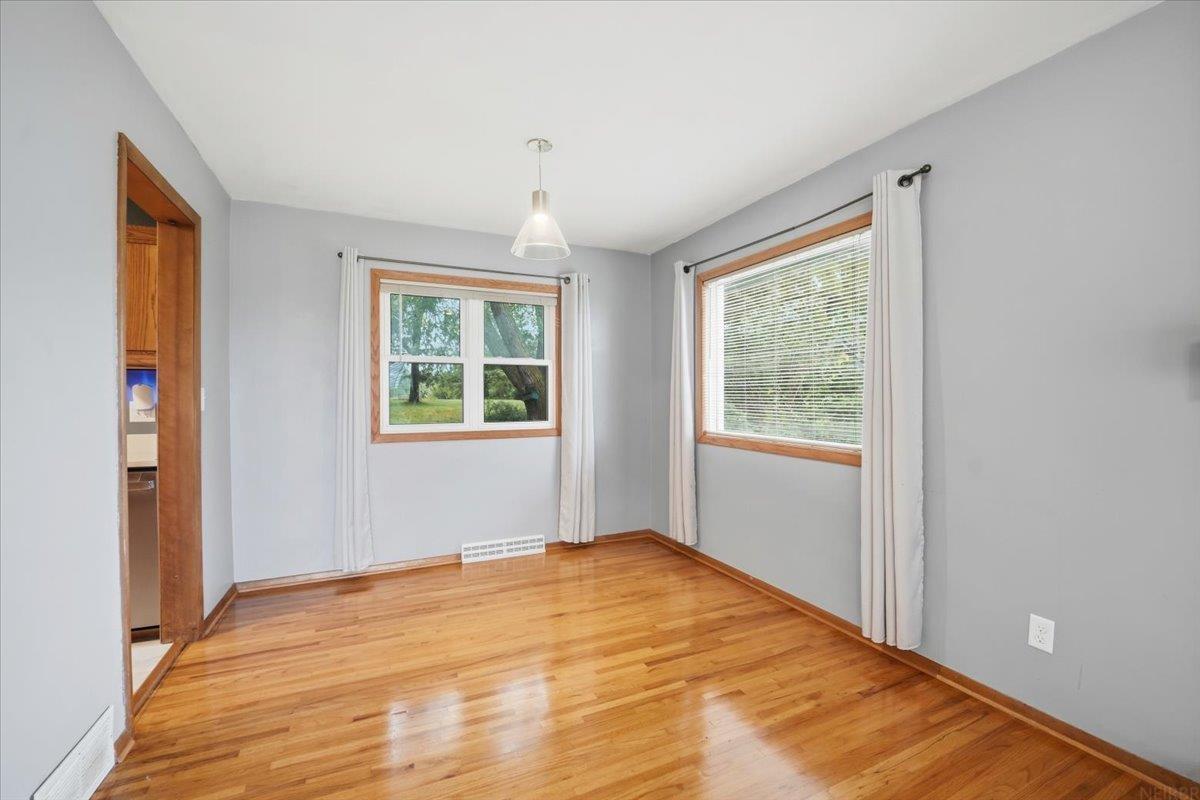 Vacant room with polished hardwood floors, two curtained windows, and a ceiling pendant light.