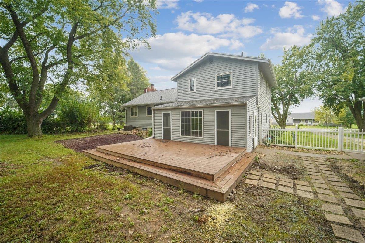Two-story gray house with a broad wooden deck and fenced backyard.