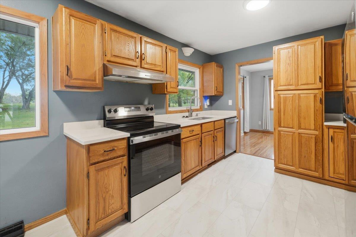 Kitchen with wood cabinets, white countertops, stainless steel appliances, and large windows overlooking the yard.