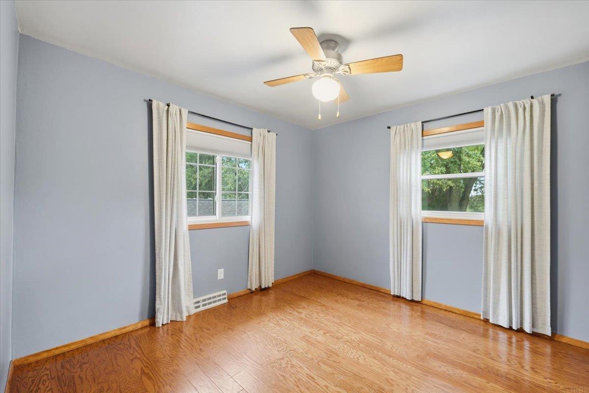 Empty room with hardwood floors, two curtained windows, and a ceiling fan with light.