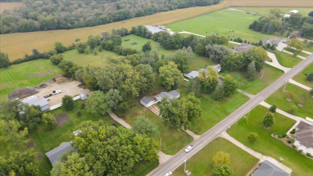 Aerial view of a tree-lined rural property beside a paved road, with open fields and several buildings.