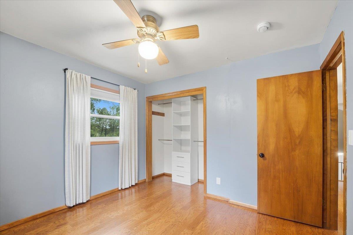 Empty bedroom with hardwood floors, an open built-in closet, and a window with white curtains.