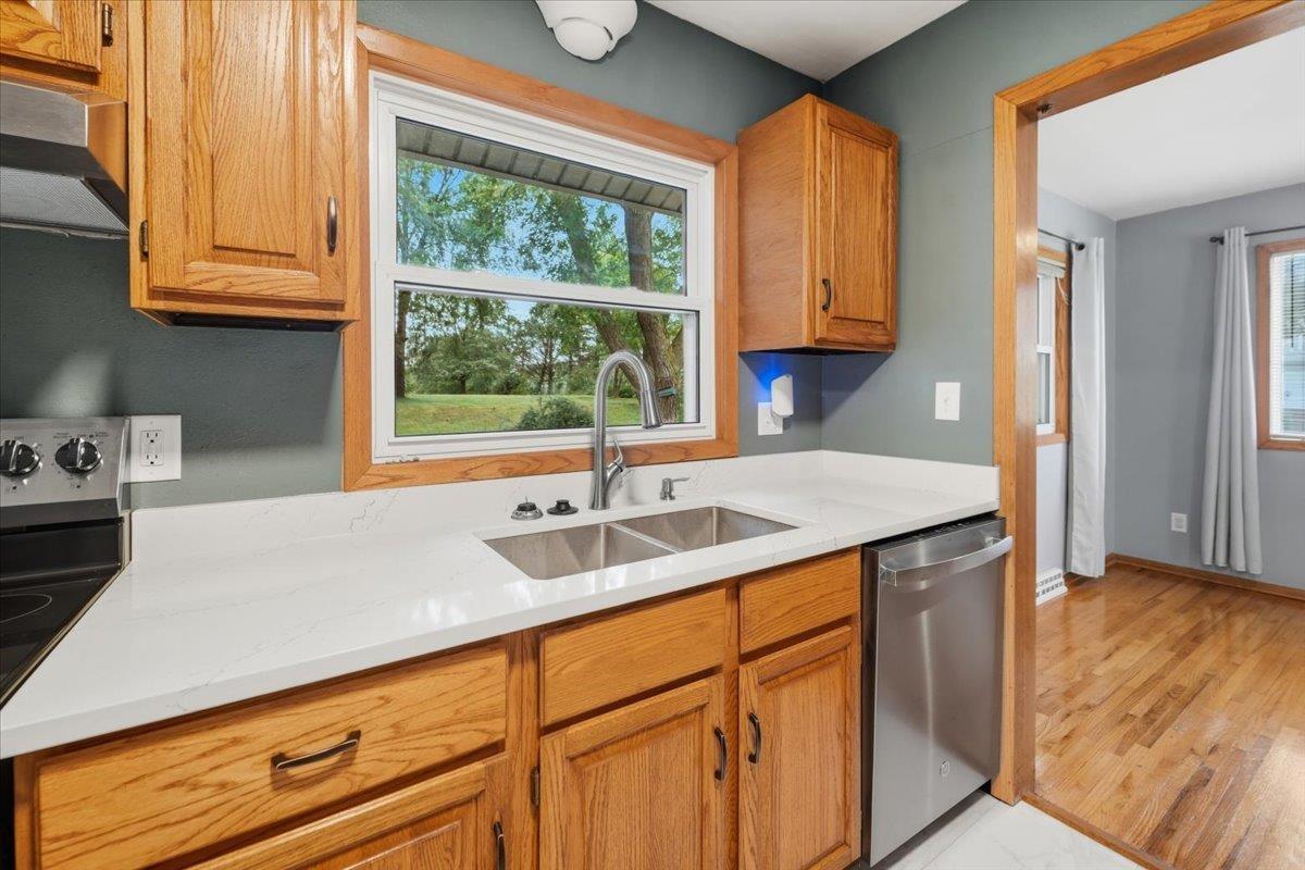 Kitchen with oak cabinets, white countertops, stainless-steel dishwasher, and a large window overlooking the yard.