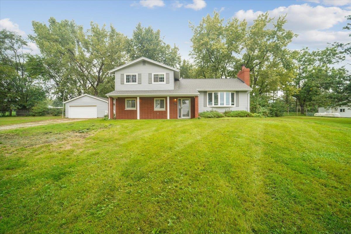Two-story brick and siding home with a detached garage and broad lawn.
