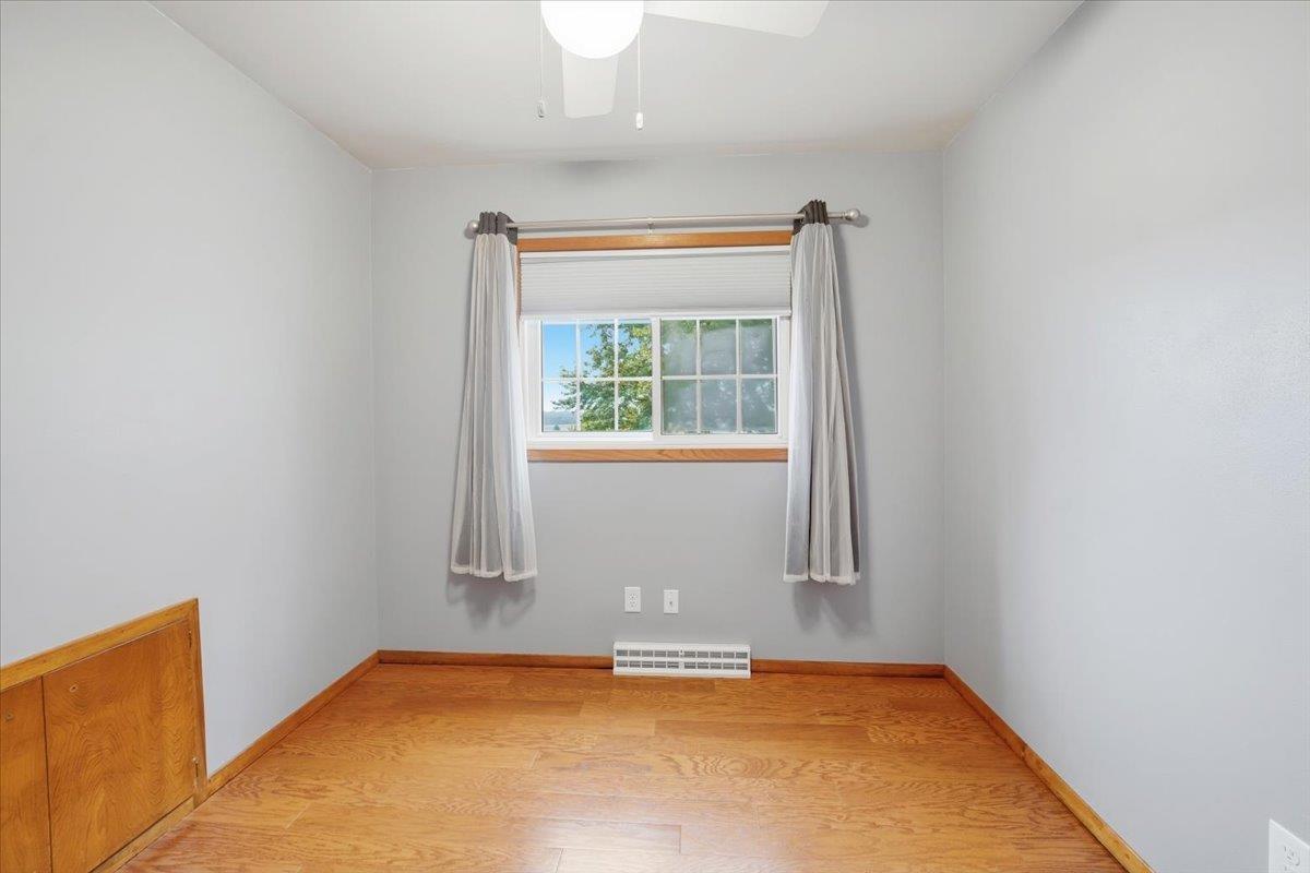Unfurnished room with wood flooring, a curtained window, and a baseboard heater.