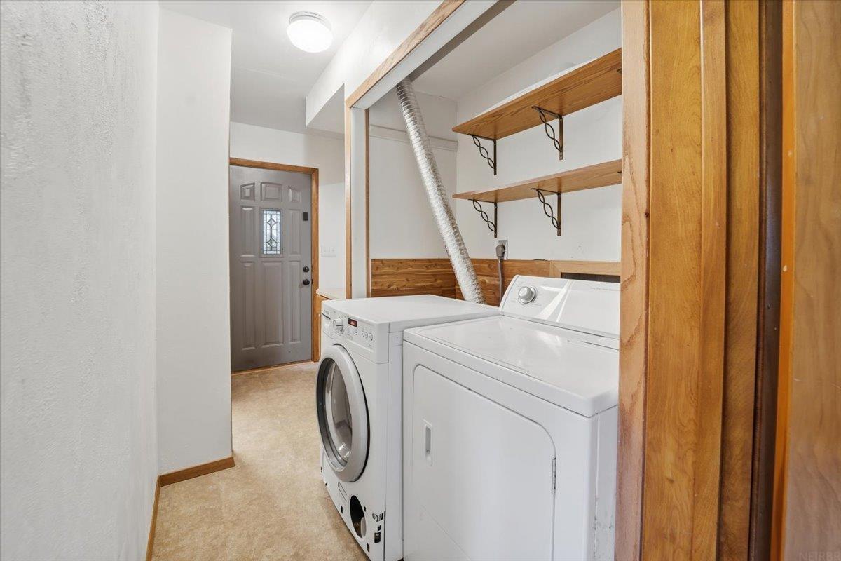 Laundry room with front-loading washer, dryer, and open wooden shelves.