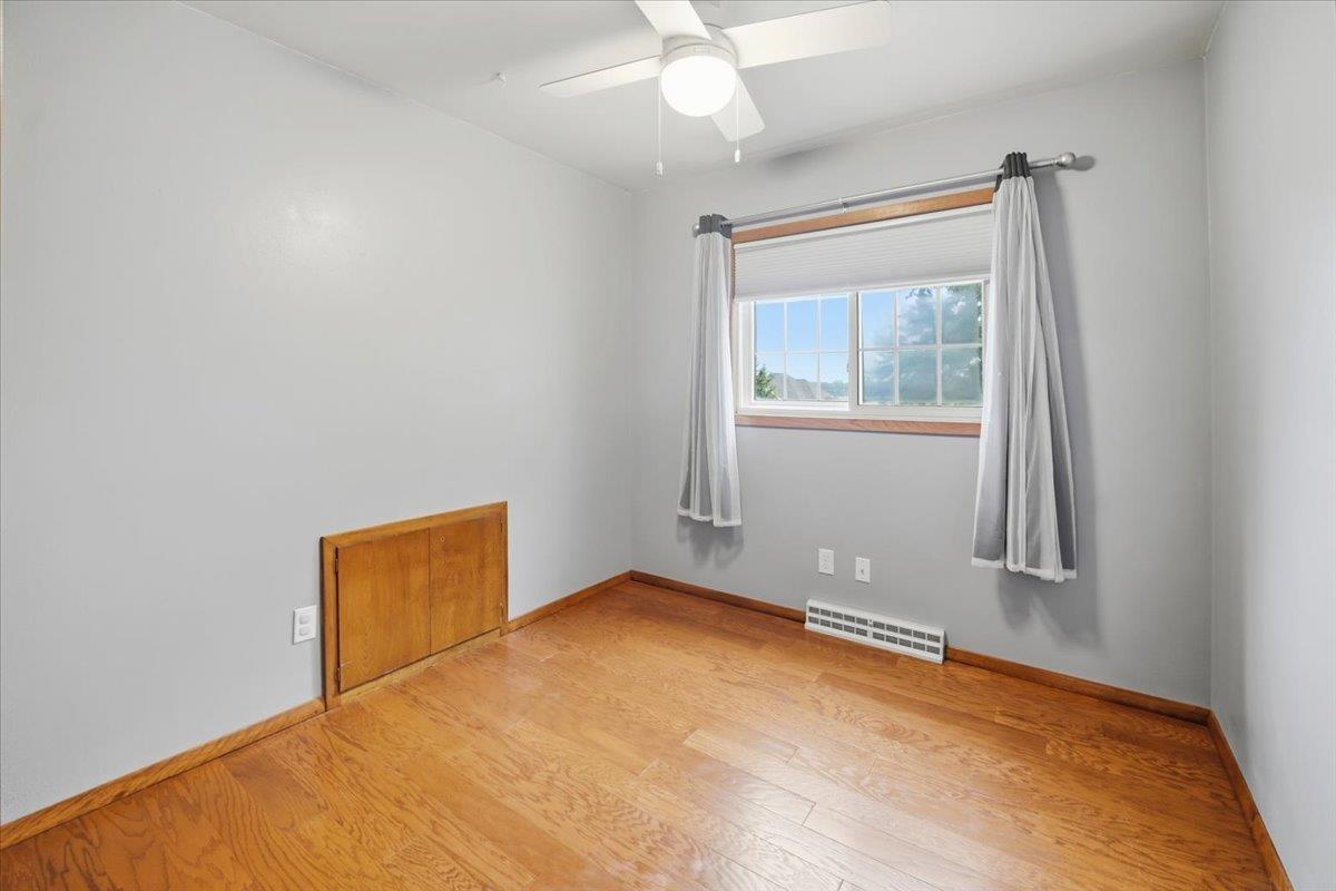 Empty bedroom with hardwood floors, wood trim, ceiling fan, and a curtained window.
