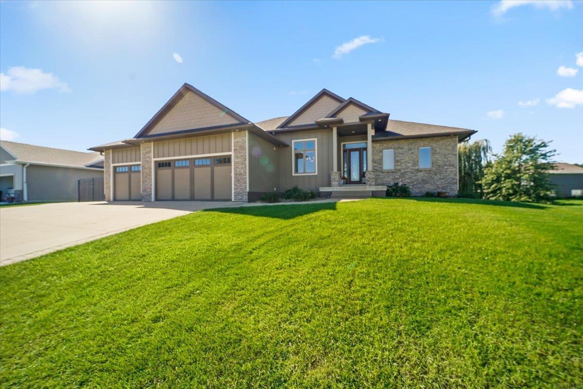 Home with stone facade, three-car garage, broad driveway, and green front lawn.
