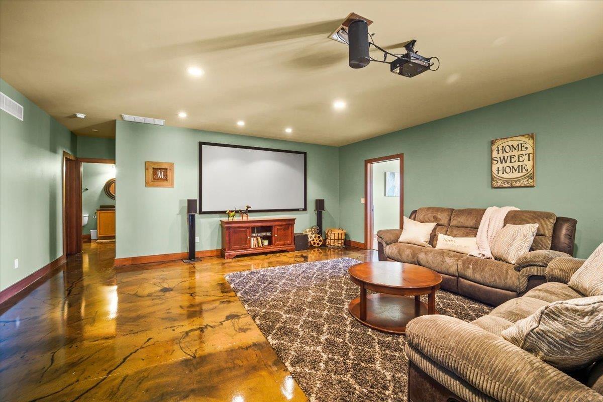 Furnished media room with a large projection screen, brown sectional seating, and glossy marbled flooring.