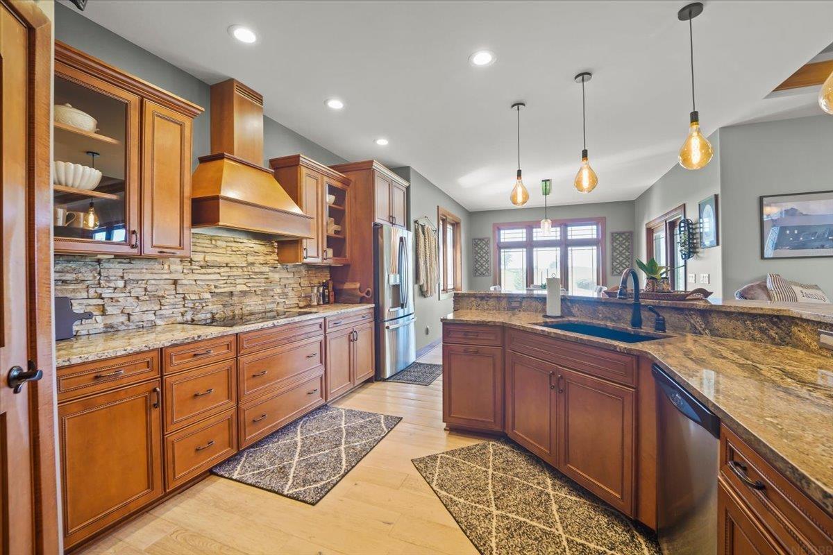 Kitchen with warm wood cabinetry, a stone backsplash, and a granite island with a sink.