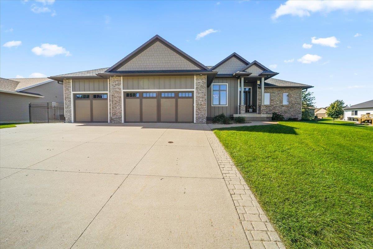 Single-story home with three garage doors, stone accents, and a broad concrete driveway.