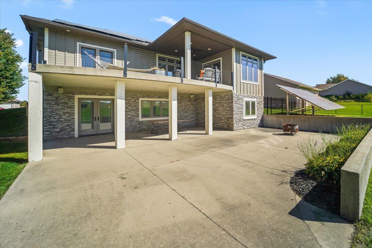 Modern home with a stone-clad patio, upper balcony, and nearby solar panels.