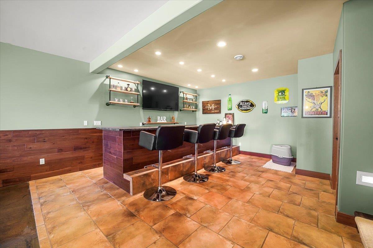 Basement bar with a wood-front counter, four black stools, and a wall-mounted television.