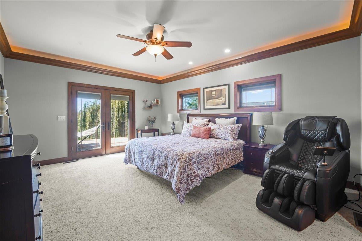 Bedroom with wood-trimmed tray ceiling, French doors, and a black massage chair.