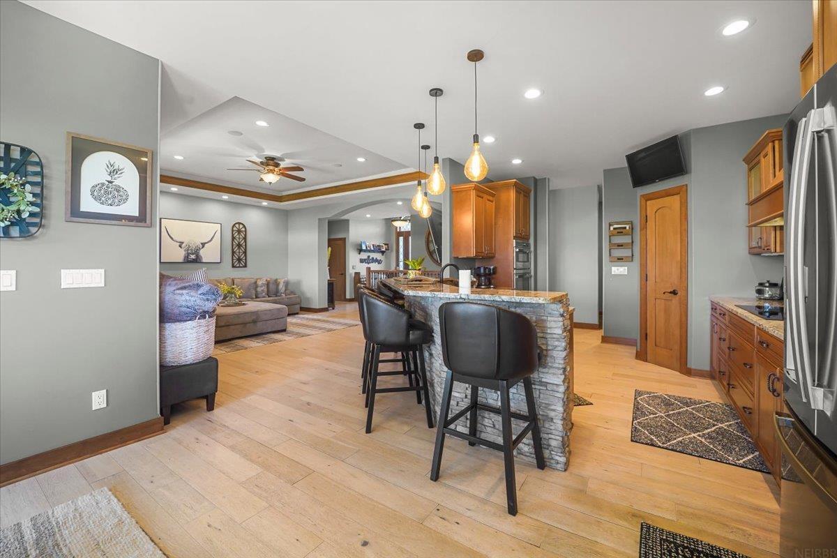Open-plan kitchen with a stone-faced island and black bar stools, adjoining a living room.