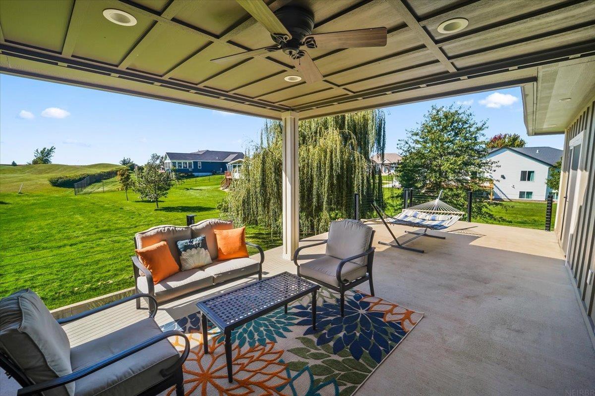 Covered patio with cushioned seating and a hammock overlooking a green lawn.
