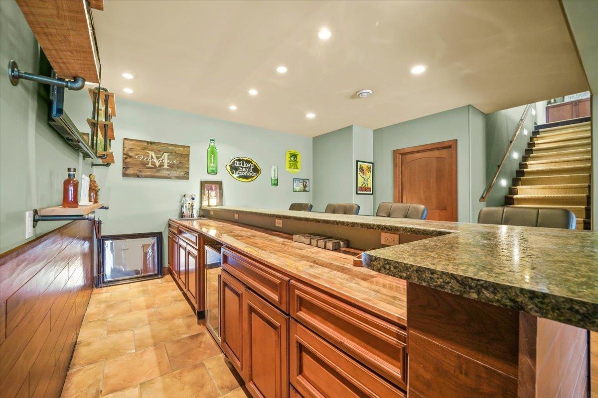 Basement bar with wood-paneled counters, granite tops, leather stools, and stairs.