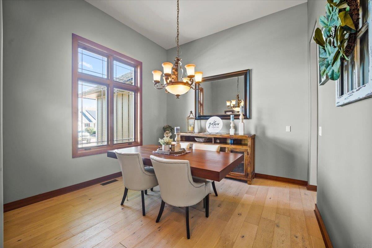 Dining room with a wood table, upholstered chairs, chandelier, and large window.
