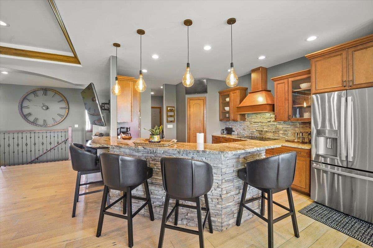 Kitchen with a large stone-faced island, bar stools, warm wood cabinetry, and stainless steel appliances.