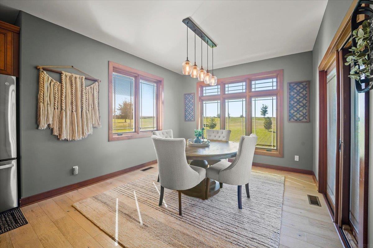 Dining room with a round table, pendant lights, and large windows overlooking open fields.