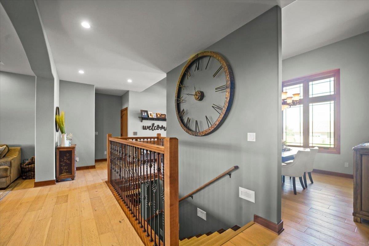 Staircase landing with wood flooring, ornate railing, oversized wall clock, and adjoining dining area.