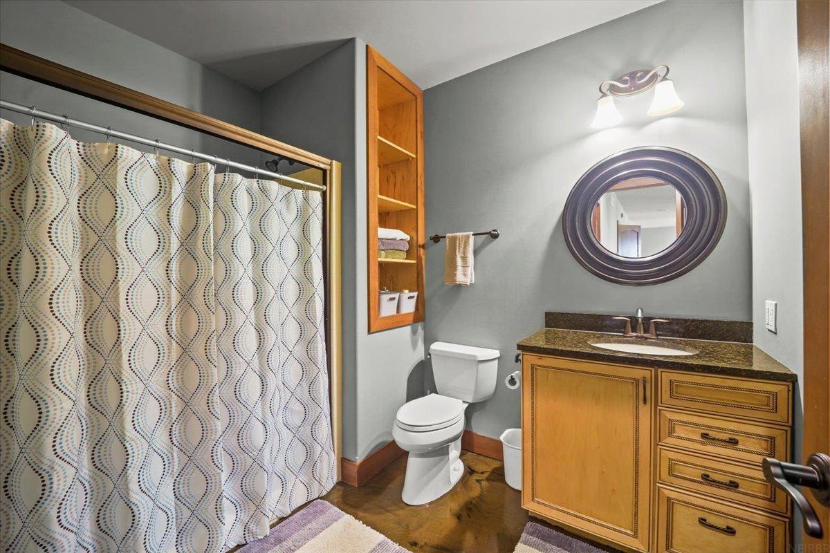 Bathroom with patterned shower curtain, wood vanity, built-in shelving, and oval mirror.