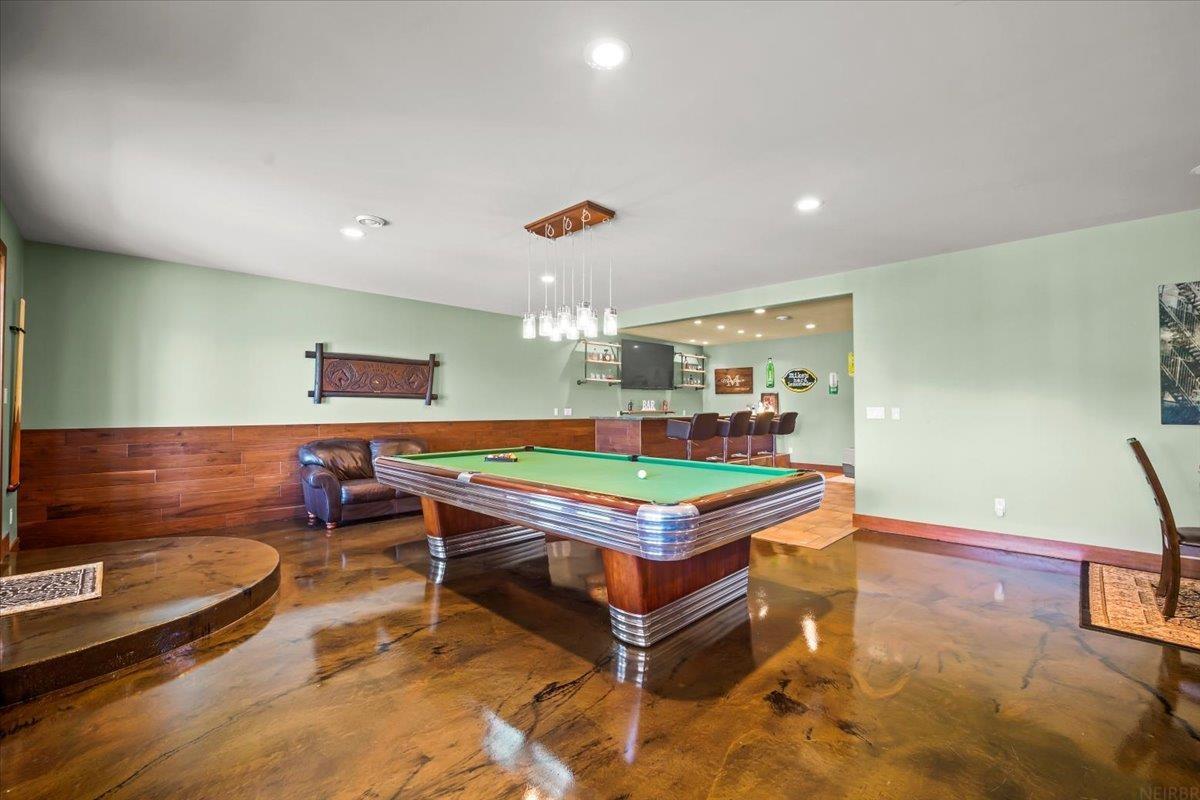 Game room with a green-felt pool table and a bar with stools.