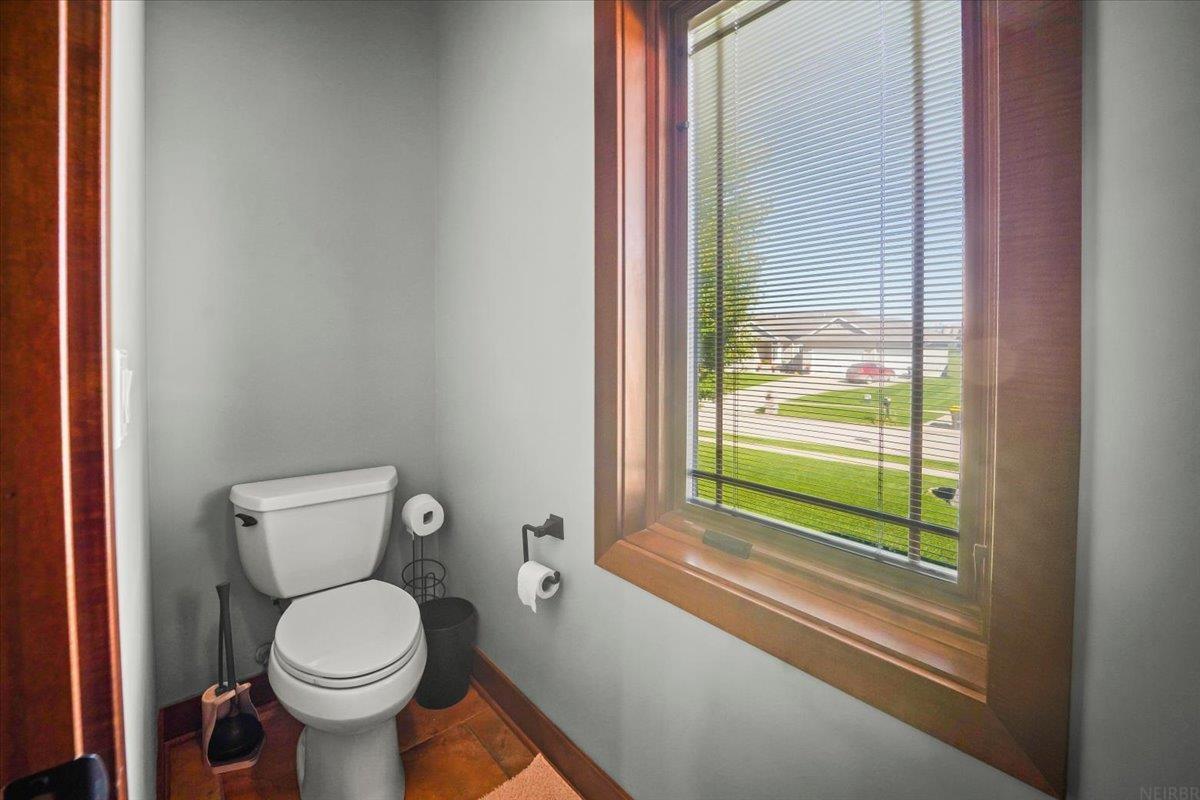Bathroom with a white toilet and a large wood-trimmed window overlooking the neighborhood.