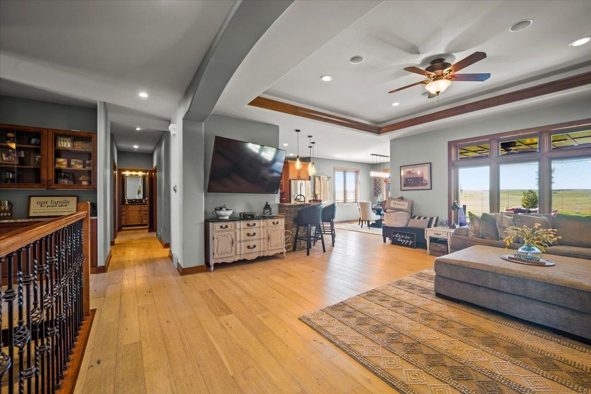Open-concept living room with a large sectional, tray ceiling, and windows overlooking open fields.
