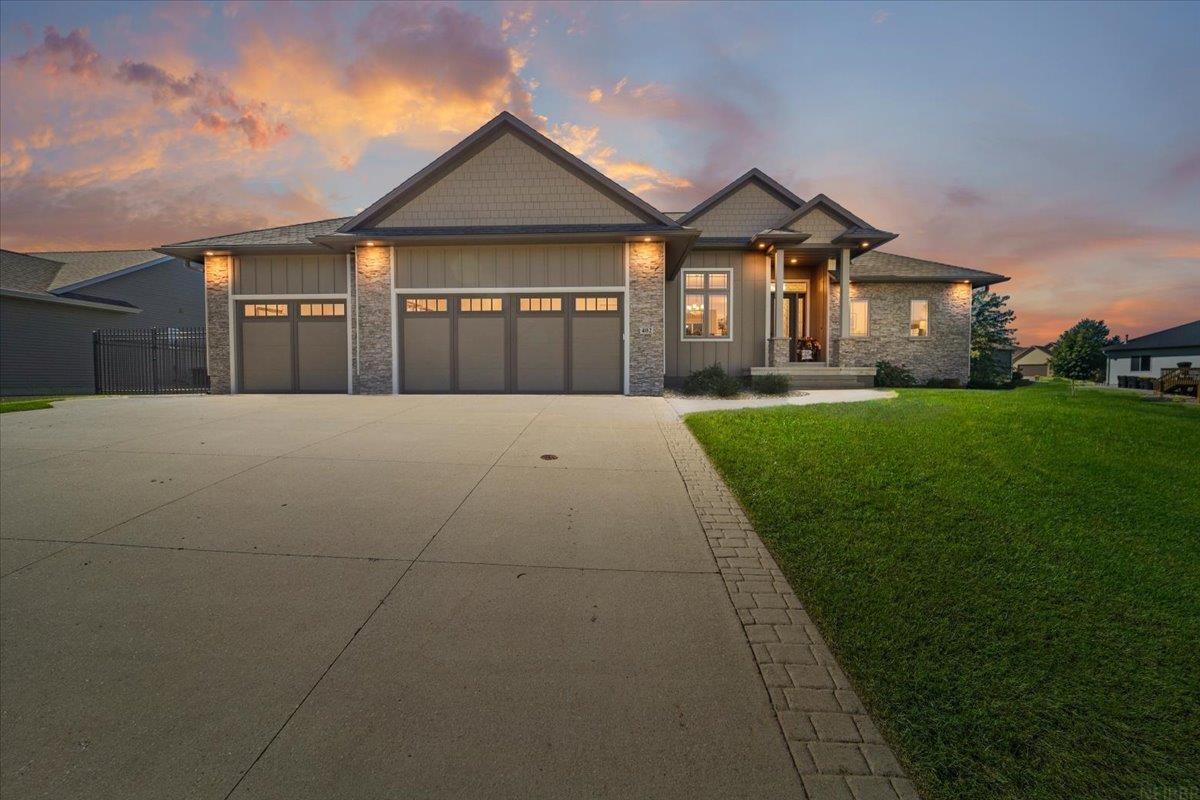Single-story stone-and-siding home with a three-car garage and broad driveway at dusk.