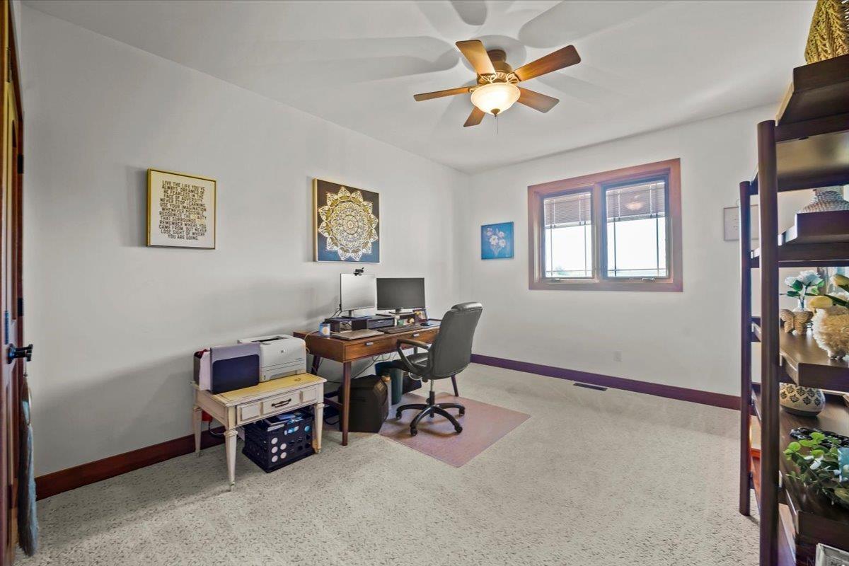 Home office with a wooden desk, dual monitors, printer, and windows with blinds.