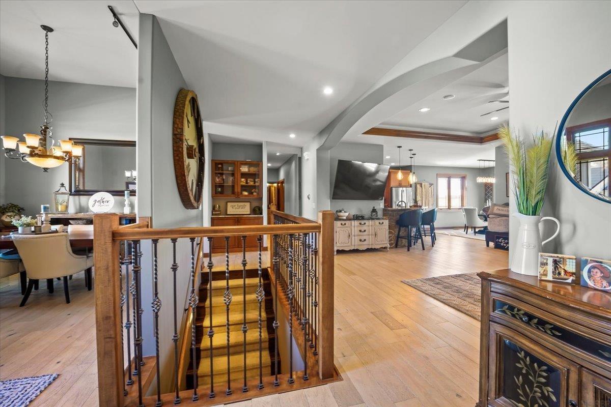 Open home interior with a wood-railed staircase, hardwood floors, and adjoining dining and kitchen areas.