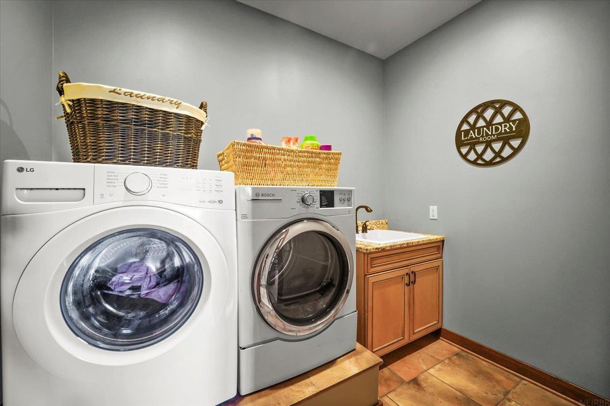 Laundry room with front-loading washer and dryer, wicker baskets, and a wooden sink cabinet.