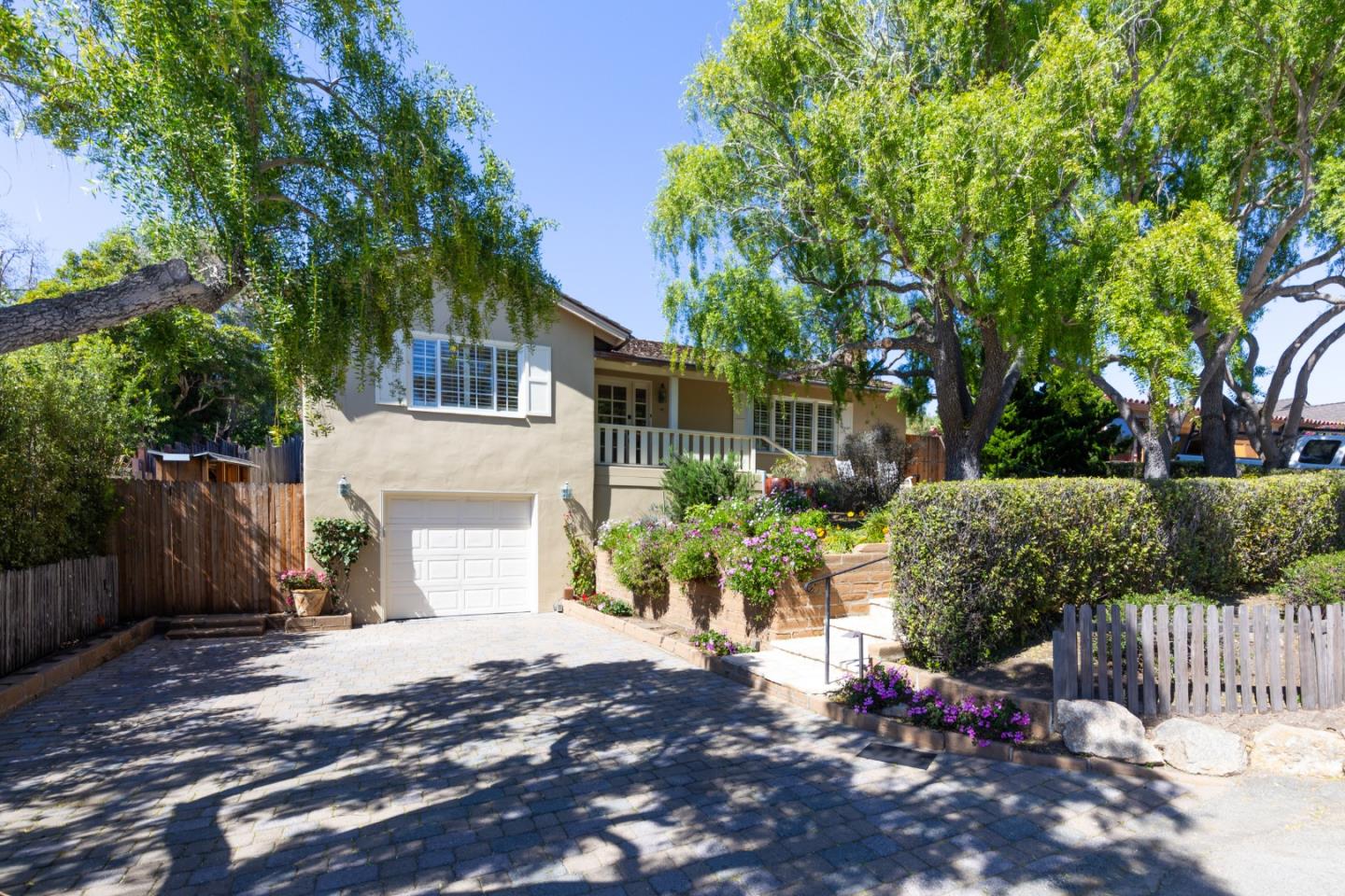 Beige home with a white garage door, covered porch, flower beds, and a broad paved driveway.