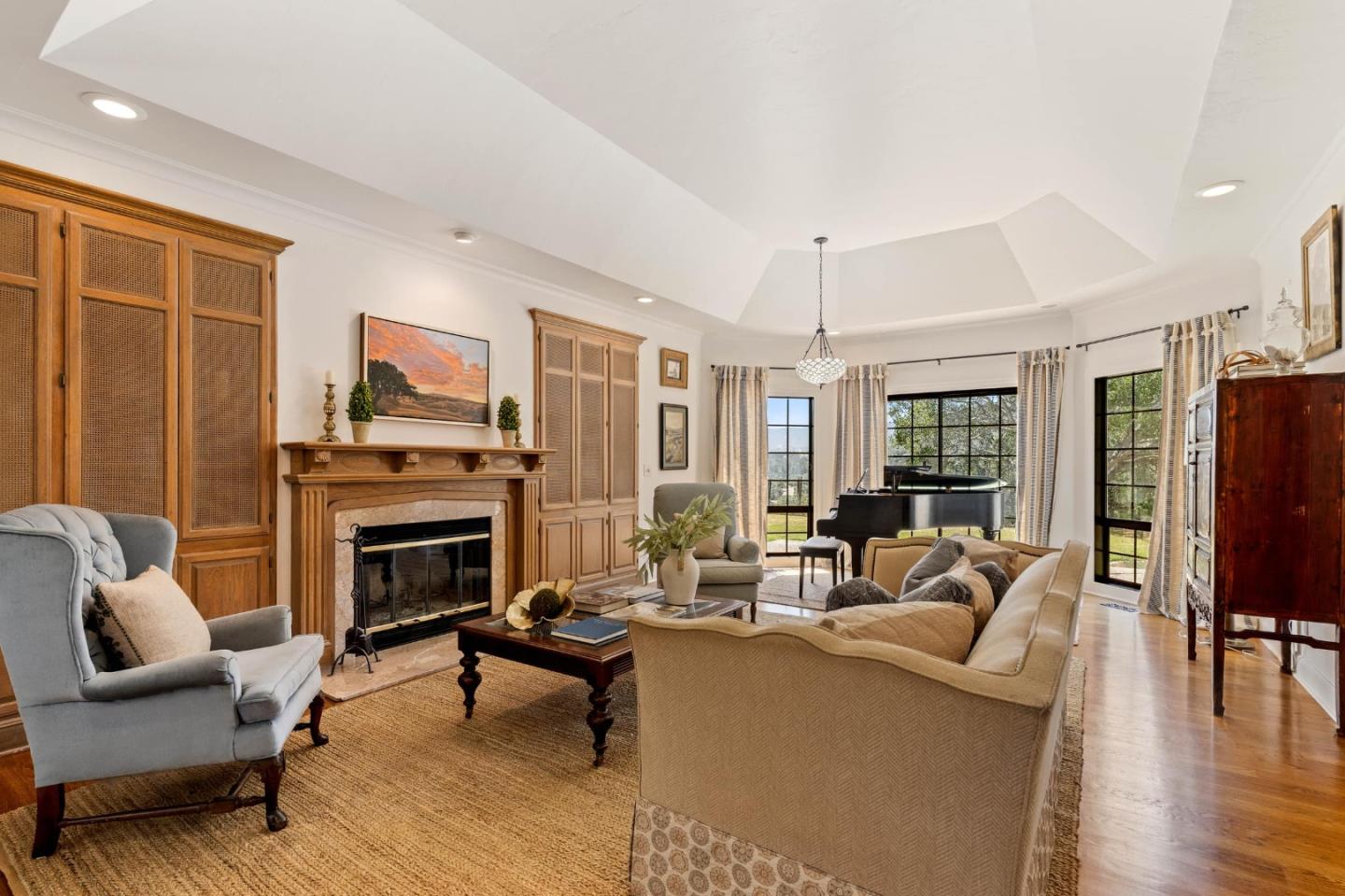 Living room with wood built-ins, a fireplace, and a grand piano by tall windows.