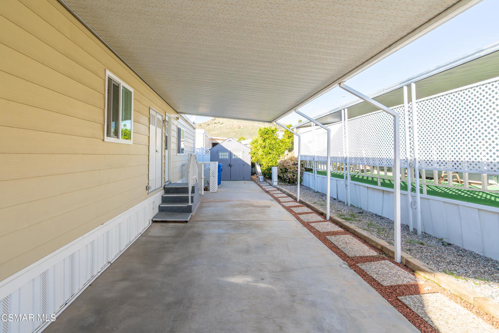 Covered concrete patio beside a beige-sided home, bordered by white lattice fencing.