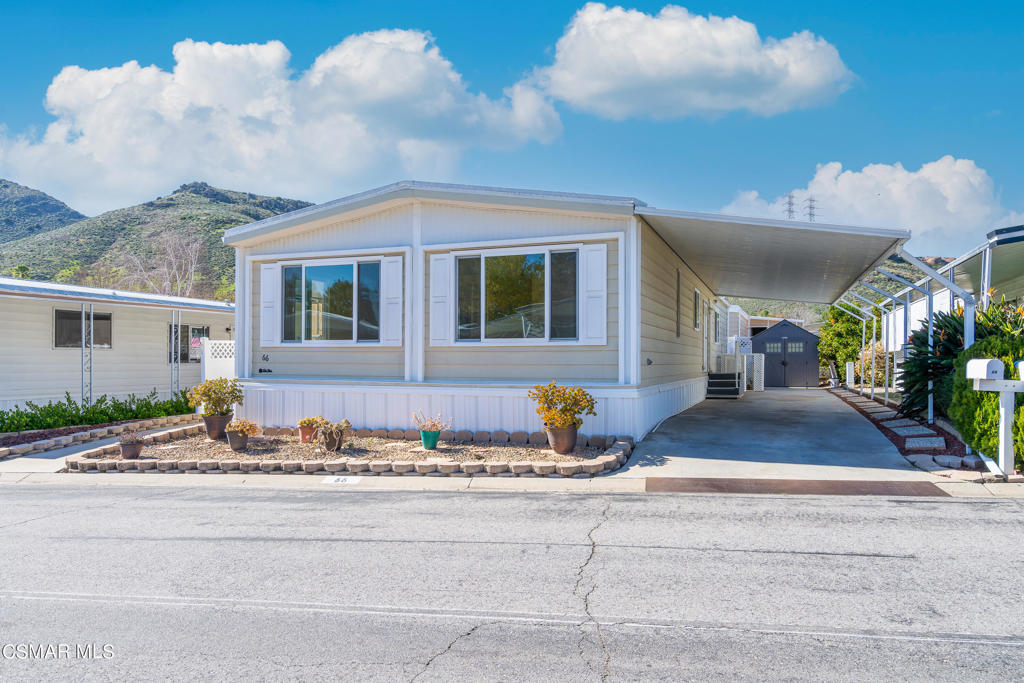 Manufactured home with a covered carport, landscaped front garden, and hills in the background.
