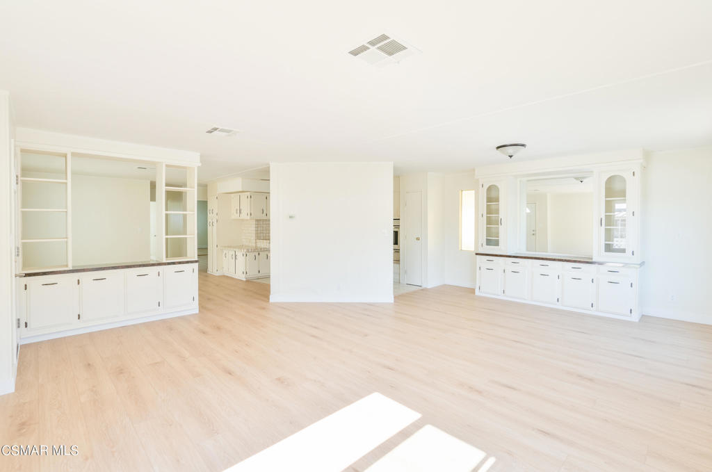 Vacant room with pale wood flooring, white built-ins, and a wide pass-through opening.