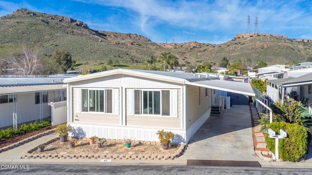 Single-story manufactured home with a covered driveway and dry hills in the background.
