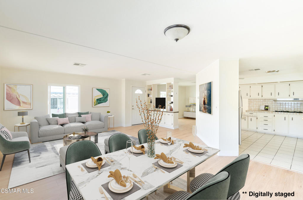 Open-plan dining and living area with a set table, green chairs, gray sofa, and white kitchen.