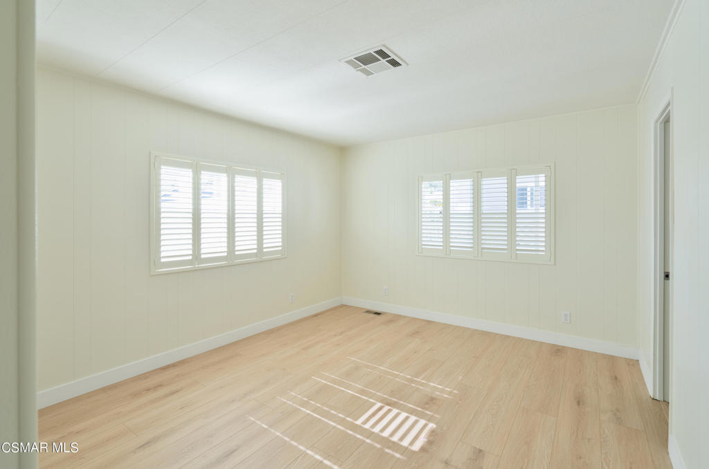 Empty room with pale wood floors and two windows with white plantation shutters.