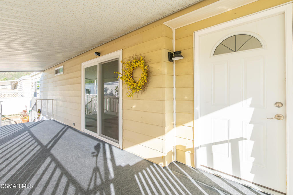 Covered porch with yellow siding, white entry door, sliding glass doors, and a floral wreath.