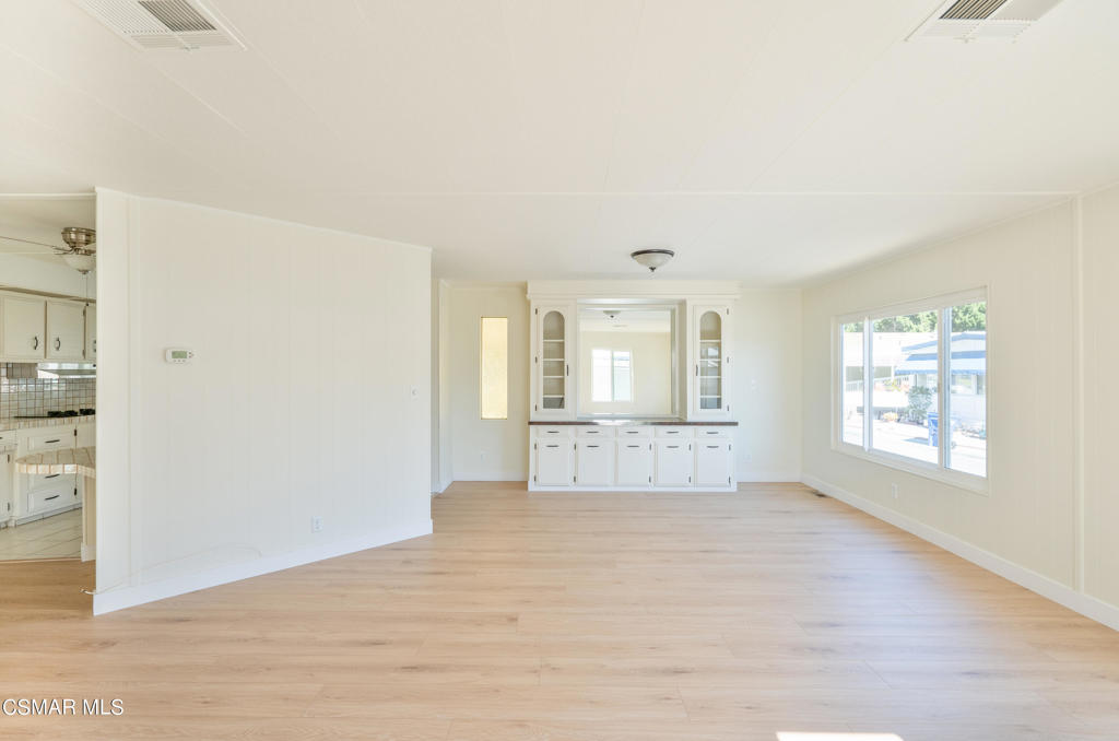 Vacant living room with pale wood floors, built-in cabinetry, and a large window.