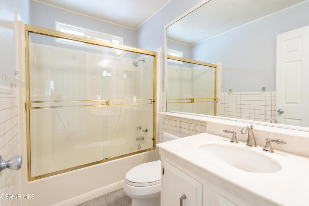 Bathroom with gold-framed glass shower enclosure, bathtub, large mirror, and white vanity.