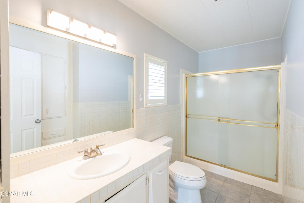 Bathroom with a long tiled vanity, large mirror, and frosted-glass shower with gold-toned trim.